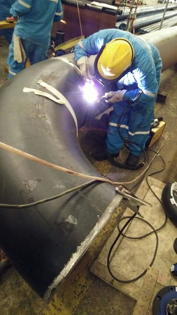 Certified welder performing TIG welding on large-diameter pipe elbow